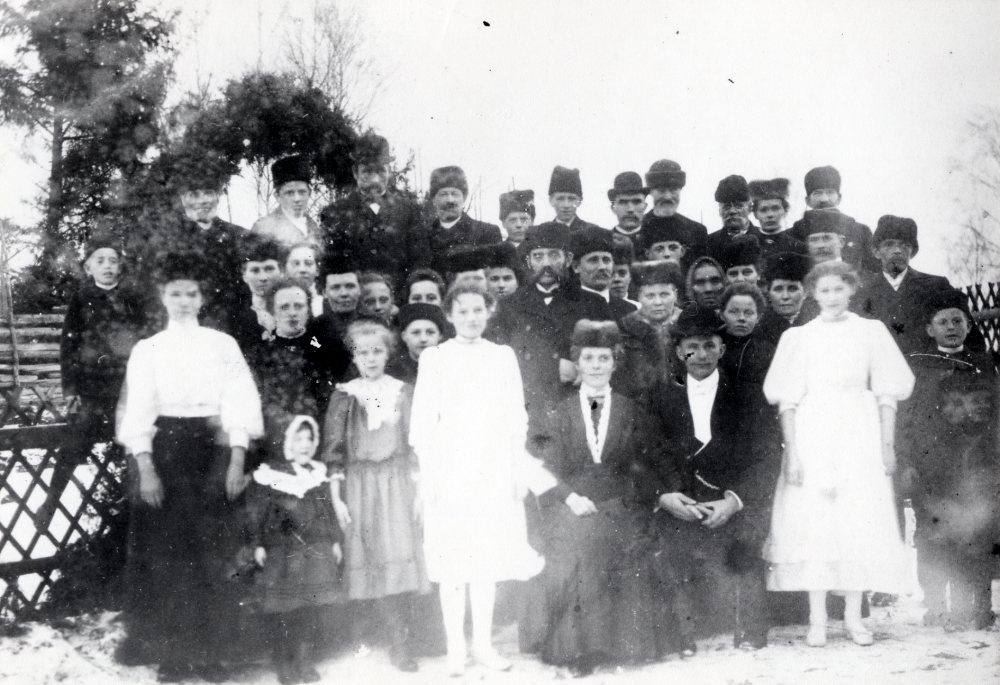 Bröllop mellan Hildur Berggren och Algot Laurell. Brudpar och bröllopsgäster har samlats utomhus vid Klippan. Brudparet är omgivna av t v tärnan Natalia Céwe och t h Linnea Pettersson.  Bakom bruden lite t v står Severin Carlsson och hans hustru.  Hildur arbetade som expediti i Severins affär, Karlbergs handelsbod