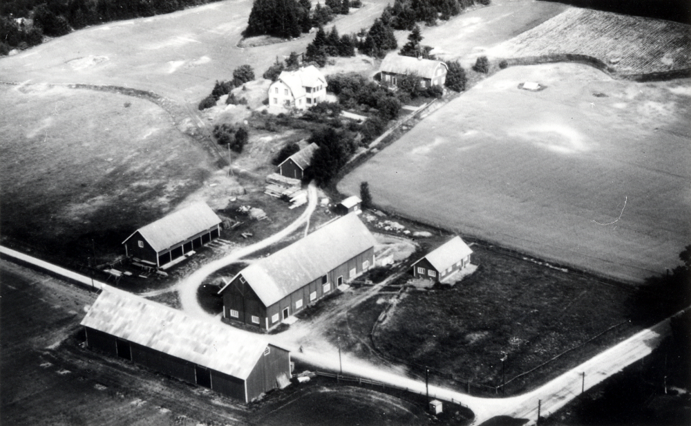 Flygfoto över Frösunda prästgårds arrendatorsbostad med ekonomibyggnader. T h går vägen från Lindholmen mot Kårsta. Den lilla vägen vid ekonomibyggnaderna går till Lilla Luttergärde