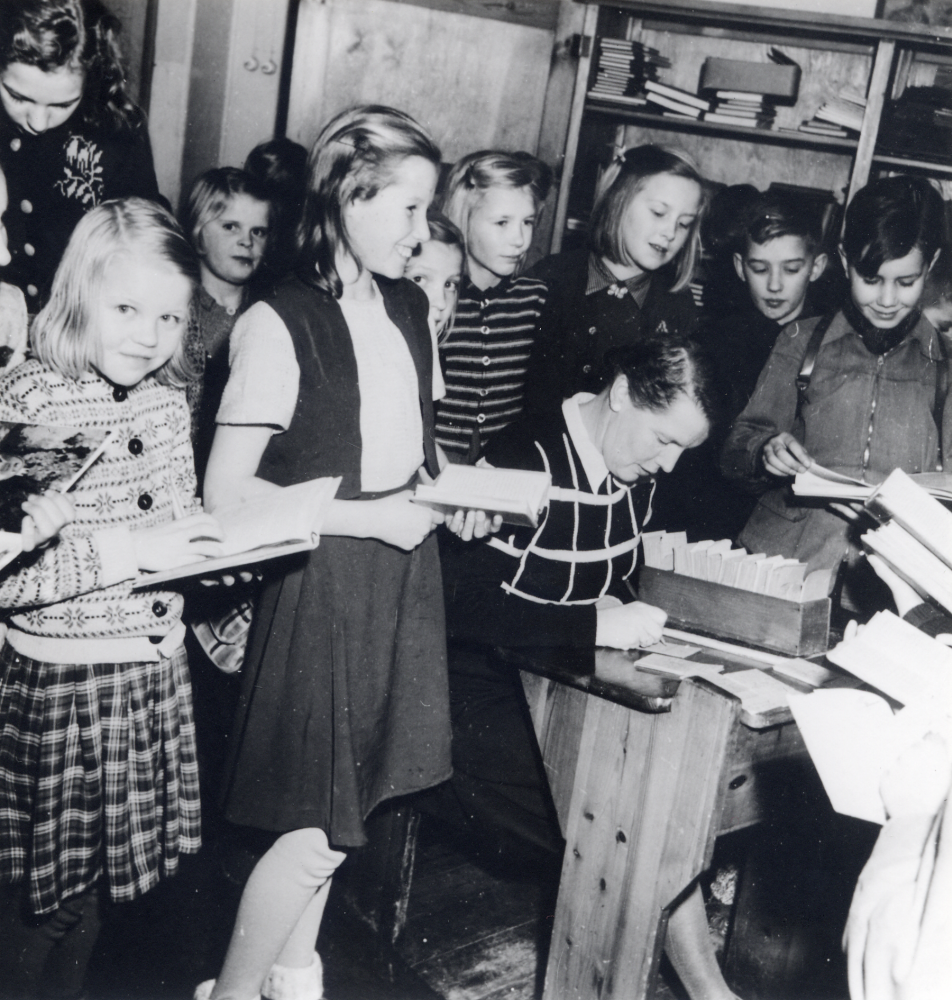 Lärarinnan Edit Lindström var den första skolbibliotekarien i Hjälmsta skola. Biblioteket tillkom på hennes och den pensionerade folkskollärarinnan Julia Fredlunds initiativ. Fröken Fredlund donerade ett startkapital till ett skolbibliotek. Här sitter Edit Lindström bland skolbarnen för att låna ut böcker. Längst t v står Jan Fridegårds dotter