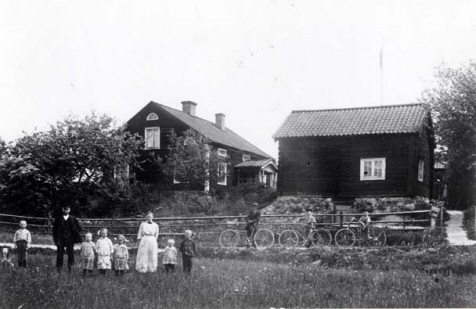 Gård. På gårdsplanen står en familj.