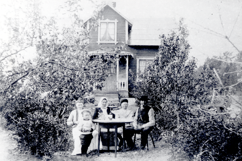 Kaffekalas på Sjöberg i Ubby, Vallentuna. Framför boningshuset sitter fr v vid bordet Alma Lovisa Jansson, född Rönn den 28 juni 1884. Hon flyttade till Stockholm 1900 och gifte sig med John Jansson, sonen Ragnar Jansson född 1907, modern Margareta Lovisa Rönn, levde 14 augusti 1855 till 25 april 1951, hon var dotter till Anders Andersson d y och Maria Margareta i Ubby. Bredvid modern Lovisa Rönn sitter yngste sonen Ruben Rönn och längst t h sitter fadern Johan August Rönn, den siste dragonen i Vallentuna.