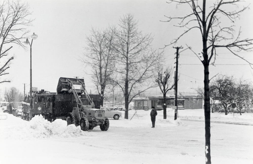Snöröjning med skoplastare vid korsningen Allévägen och Banvägen.  I bildens mitt syns Pressbyråns kiosk norr om Vallentuna station