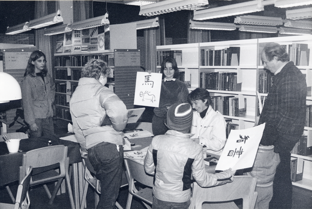 Skrivarverkstad i Vallentuna bibliotek. Vid bordet står Lena Werner, verksam vid ostasisatiska museet och visar hur man skriver kinesisk skrift och låter besökarna själva pröva på
