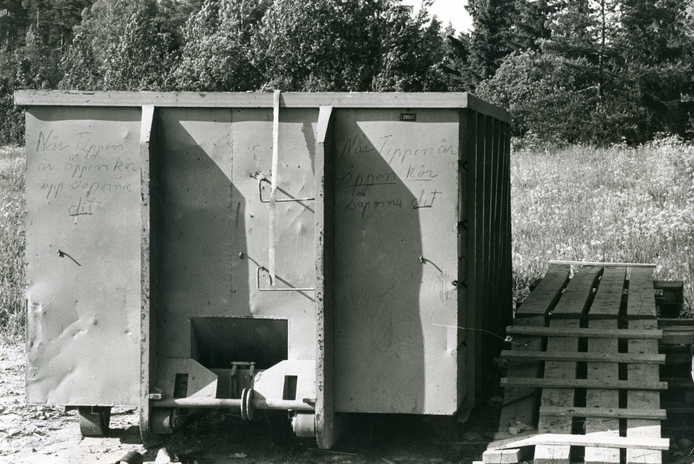 Sopcontainer uppställd ndanför Högdalatippen.  Textat på containern, "När tippen är öppen, kör upp soporna dit"
•Fotografiet ingår i bildserien ”Vardagsliv i Vallentuna kommun” av Rachael Gough-Azmier & Gunilla Blomé, Haga Studios HB.
