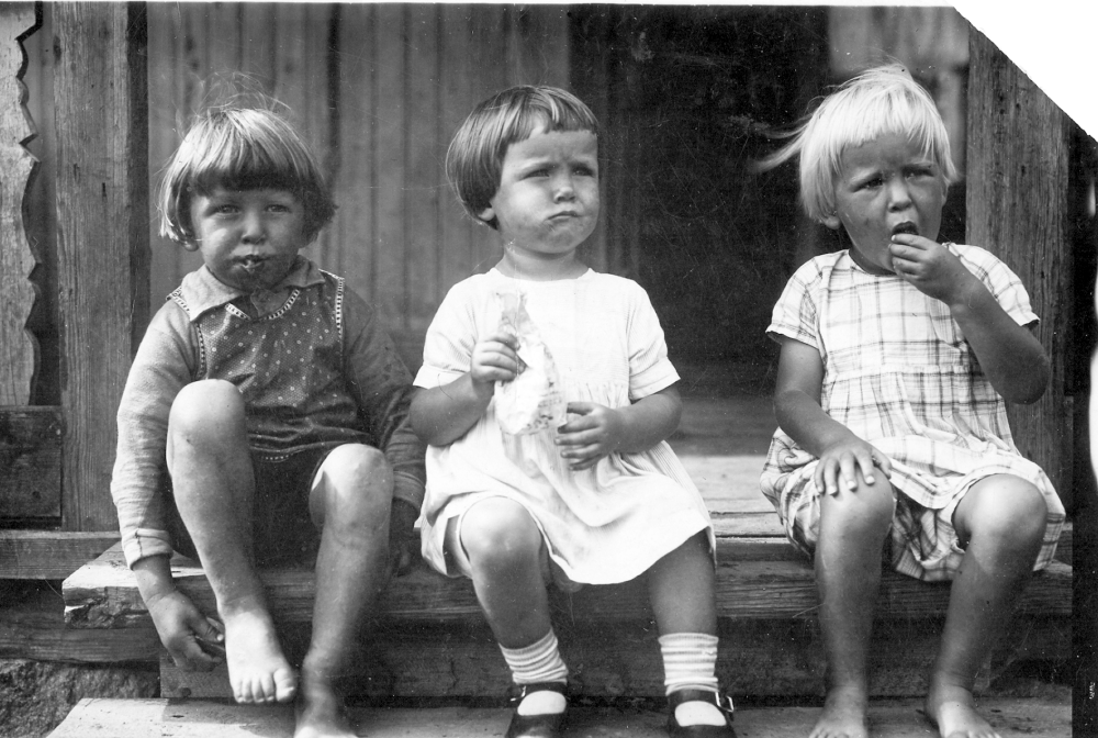 Barnen Erik Eriksson, Ingrid och Marianne Hamberg sitter på trappan till Påtåker och kalasar på godis som de fått som gåva. Barnens munnar är alldeles fulla, för det har berättats att det gällde att äta upp allt godis så snabbt som möjligt