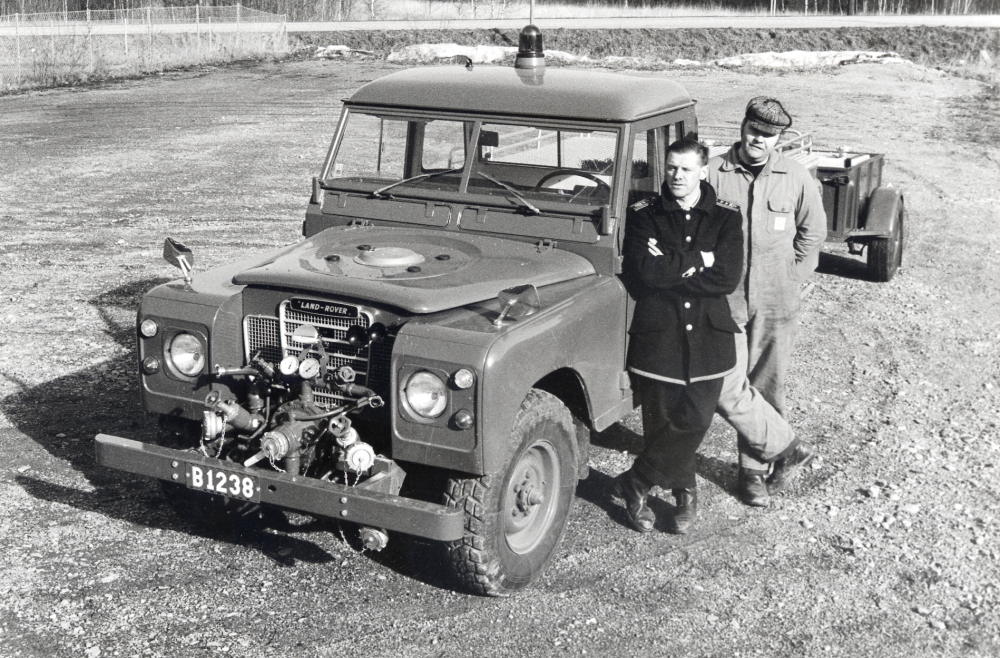 Brandchef Bertil Malmström och Bengt Berg (son till Agne) står bredvid den nyinköpta jeepen  med registreringsnummer B 1238  på parkeringsplatsen utanför gamla brandstationen vid Olsborgsvägen.  Fotografen Jan Ek krockade med jeepen sedan han fotograferat en brand i Tärnan området.  Hans Fiat blev bara skrot.  Jeepen öde är okänt!