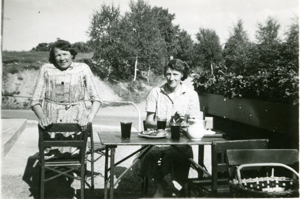 Olga Axén och Anna-Lisa på uteserveringen, Angarns café. Bakom Anna-Lisa går vägen upp till Alby. Anna-Lisa var servitris och allt i allo. Bakom Olga ligger ”Kärlekskullen”, senare Anderssons Industri.
Begsättra i Angarn med café och Shell bensinstation drevs av Seth Abel Axén (levde 1899-1986) tillsammans med hustrun Ruth (1904-2003) samt systern Olga Axén (död 1951). Seth började med en kiosk på 1930-talet. 1947 byggdes fastigheten om.