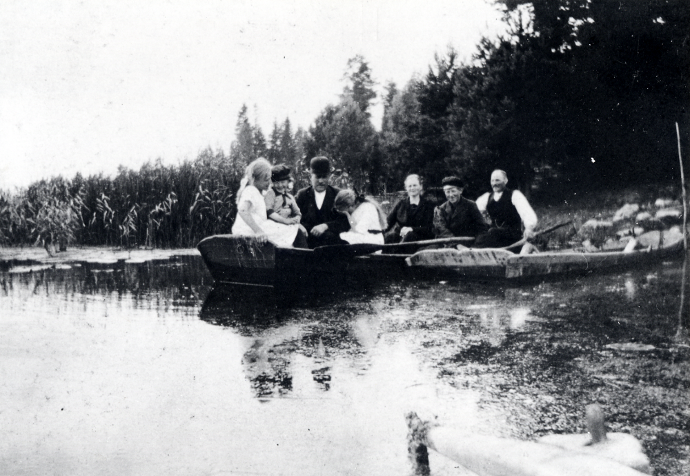 Roddbåt i Stolp-Ekebysjön Frösunda.  Båten ligger vid stranden och i båten sitter 2 män, 1 kvinna, 3 småflickor och en pojke
