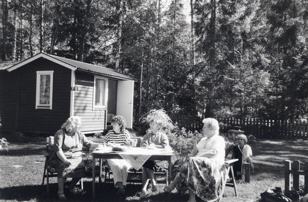 Personalen vid Vallentuna bibliotek har gjort studiebesök på Norrtälje bibliotek inför den planerade datoriseringen. Efteråt bjuder Eivor Tillborg på kaffe i sitt sommarhus vd sjön Erken.  Vid kaffebordet sitter fr v Inger Olsson, Ulla-Britt Kvarnestam, Anna Aspenström och Anitha Gräns.  På marken t h sitter Anna Brynell