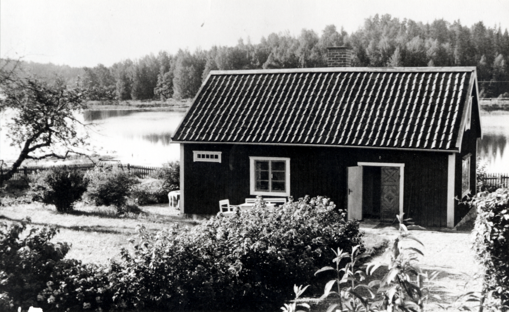 Lillstugan vid Helgö gård.  Elin Johansson, maka till gårdens ägare Emanuel Johansson, gav pengar till driften av Lillstugan som skulle vara en gemensam samlingsplats för de 13 syskonen Helgöstam.  I bakgrunden syns Helgösjön.  Lillstugan kallas "Per Mats" efter Per Mattson som tidigare varit delägare i gården