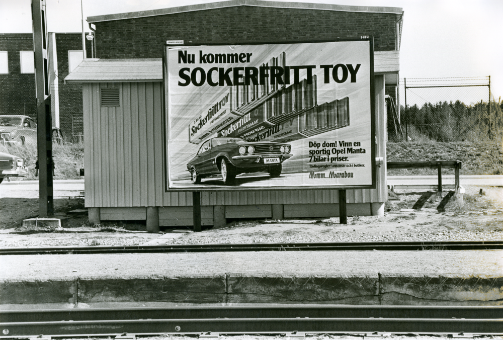 Reklamskylt vid Vallentuna station våren 1973. "Järnvägs-reklam 212". 
•Fotografiet ingår i bildserien ”Vardagsliv i Vallentuna kommun” av Rachael Gough-Azmier & Gunilla Blomé, Haga Studios HB.
