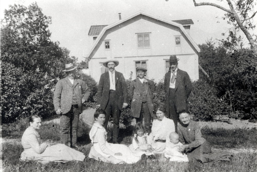 Lövhamra gård i Össeby-Garn. Utanför mangårdsbyggnaden står fr v Verner Holmström, okänd, okänd, ev Carl Johansson (1882-1926) och okänd. Sittande fr v Johanna Pettersson, Konstans Holmström, flickan med flätor är Tyra Holmström *1904, Axelina Johansson, det lilla barnet Arne Johansson och Gerda Johansson