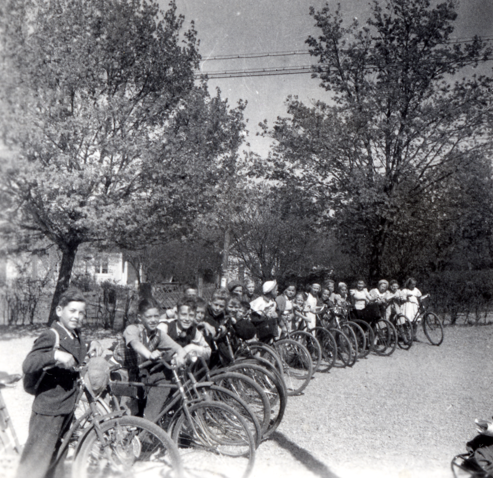 Skolbarn från Hjälmsta skola samlade på skolgården före en cykelutfärd. Hembygdsundervisning och idrottsutövning kombineras vid de cykelutfärder som var vanliga under 1940-talet.