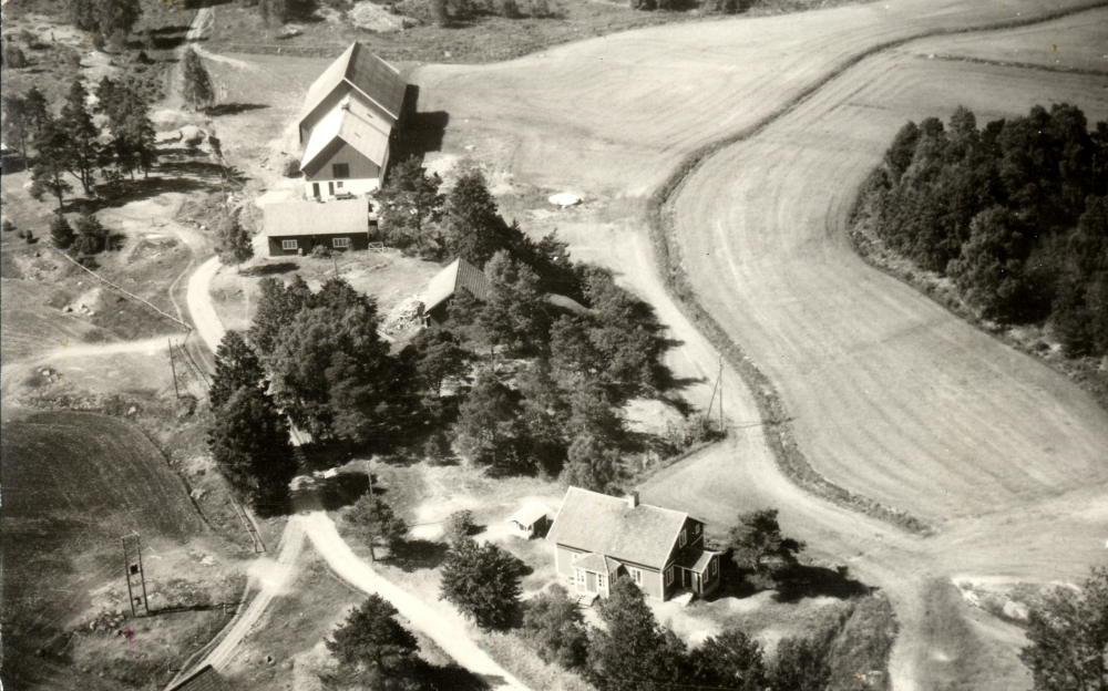 Flygfoto över arrendatorbostaden vid Össeby-Garns prästgård.  Längst bort finns ladugård, byggd på 1950-talet, och hönshus.  Magasinets tak skymtar bland träden och i förgrunden ligger bostadshuset