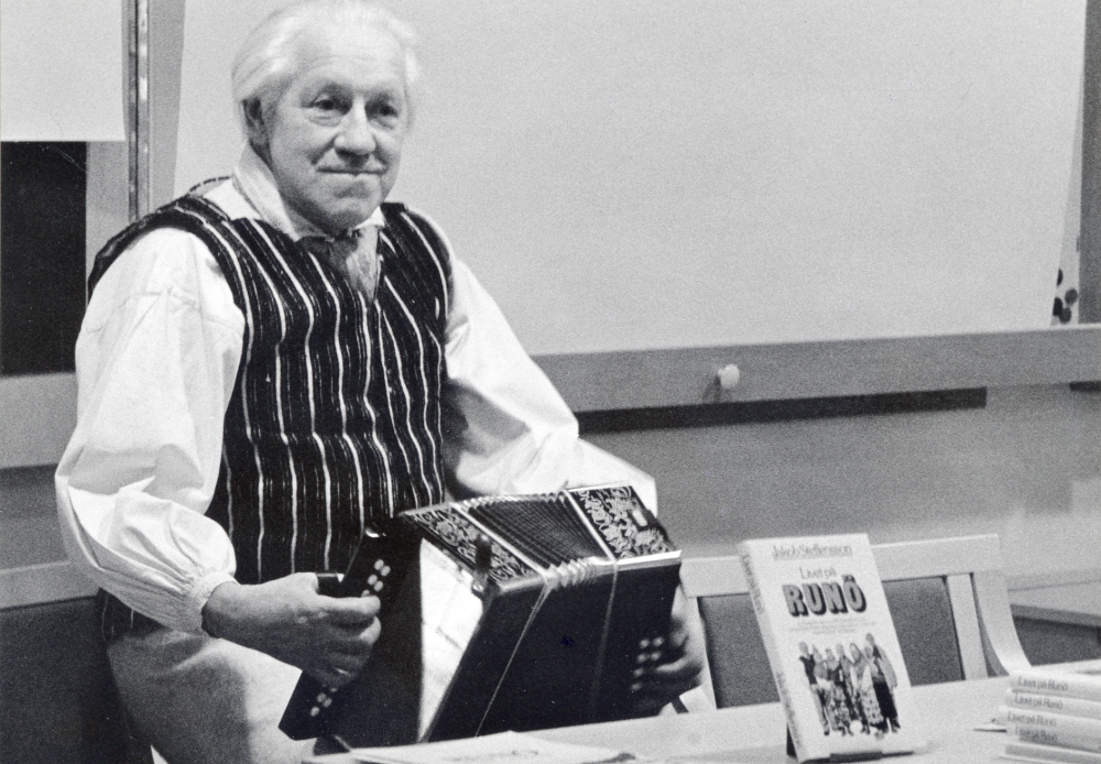 Runö, svenskön i Rigabukten, en utställning i Vallentunasalen 4-16 mars 1985. Jacob Steffensson, som själv kommer från Runö, berättar och visar bilder i anslutning till utställningen i programmet Kring svenskön Runö. Här sitter föredragshållaren med ett handklaver och framför honom på bordet står boken han skrivit: Livet på Runö