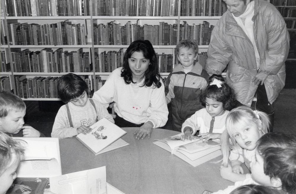 En grupp barn från  Granåsa daghem  besöker  Vallentuna bibliotek  och tittar i bilderböcker på barnavdelningen. Vid bordet sitter   Laleh Toosie  som bl a har hand om de persisktalande barnen, och t h står  Gun-Britt Gustavsson