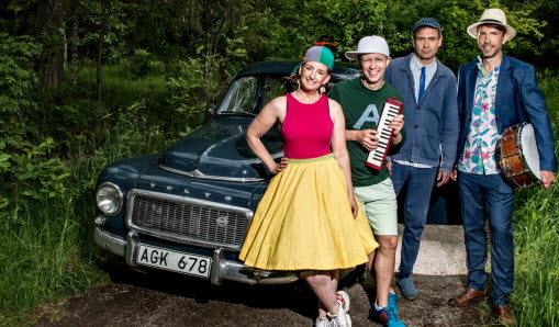 Artister på scenen med publik i bakgrunden.