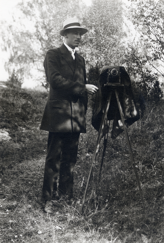 Amatörfotografen Birger Regny, Birger Pettersson från Granby gård i Össeby-Garn samarbetade med Algot Laurell från Frösunda. Birger Regny levde 1891-1968. Han var chaufför och arbetade först hos Freys hyrverk innan han bildade ett eget bolag, Packard hyrverk. På bilden står Birger Regny med kamera på stativ med svart skynke över iklädd kostym och hatt. Birger var son till Frans Albert Pettersson och Amanda Gustafsson från Skrävsta. Han växte upp i Granby tillsammans med syskonen Edvard och Linnea. Linnea arbetade före sitt giftermål som växeltelefonist i Brottby.