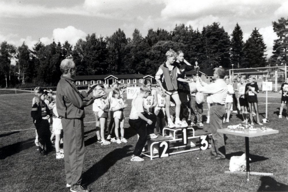 Jubileumsklubbmatch i friidrott mellan Brottby SK och Vallentuna Friidrottsklubb  på Össeby idrottsplats 12 september 1998.  Alla deltagare fick guldmedalj.  Maria Åberg och Johan Svensson tar emot segerpokalen av Jan-Åke Bredberg, fritidschef i Vallentuna.  T v i träningsoverall står Rolf Öhrneman som låtit någon låna hans kamera för fotot