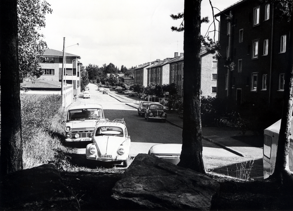 Fornminnesvägen sedd från väster mot öster och Mörbyvägen.  På vägens vänstra sida syns bostadshusen i bostadsrättsföreningen Granen, byggda 19666/67.  I bakgrunden syns ännu gammal bebyggelse vid Mörbyvägen. Bilar är parkerade vid vägens slut, t ex 2 Volkswagen, en Ford Transit och förmodligen en Chrysler