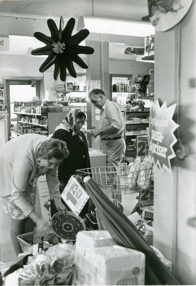 Sista dagen för handlarfamiljen Karlsson i Frösunda handel. Seth Karlsson och två kunder i butiken.
•Fotografiet ingår i bildserien ”Vardagsliv i Vallentuna kommun” av Rachael Gough-Azmier & Gunilla Blomé, Haga Studios HB.
