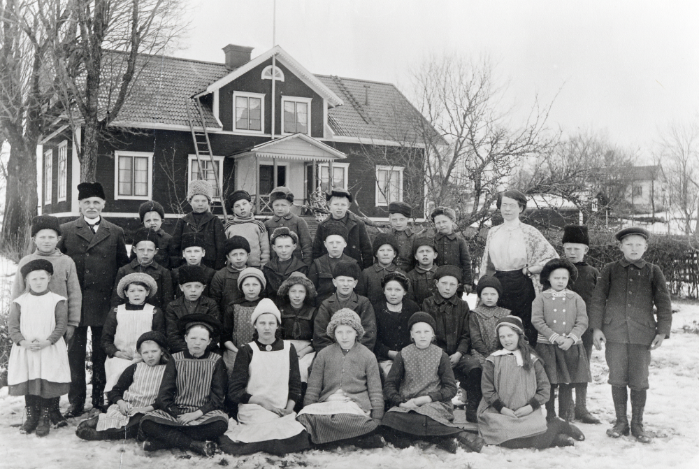 Skolbarnen samlade utanför Angarns kyrkskola.  T h står lärarinnan Ida Solem.  Den lilla flickan stående längst t h är Karin Lundin, senare gift Edman, dotter till Nanna Lundin i Karlborgs handel
