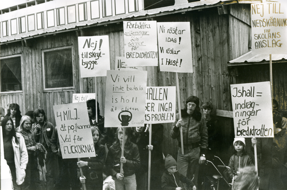 Inför kommunfullmäktiges sammanträde och debatt om femårsplan och ishall i Vallentuna pågår demonstrationer ute på torget.
•Fotografiet ingår i bildserien ”Vardagsliv i Vallentuna kommun” av Rachael Gough-Azmier & Gunilla Blomé, Haga Studios HB.
