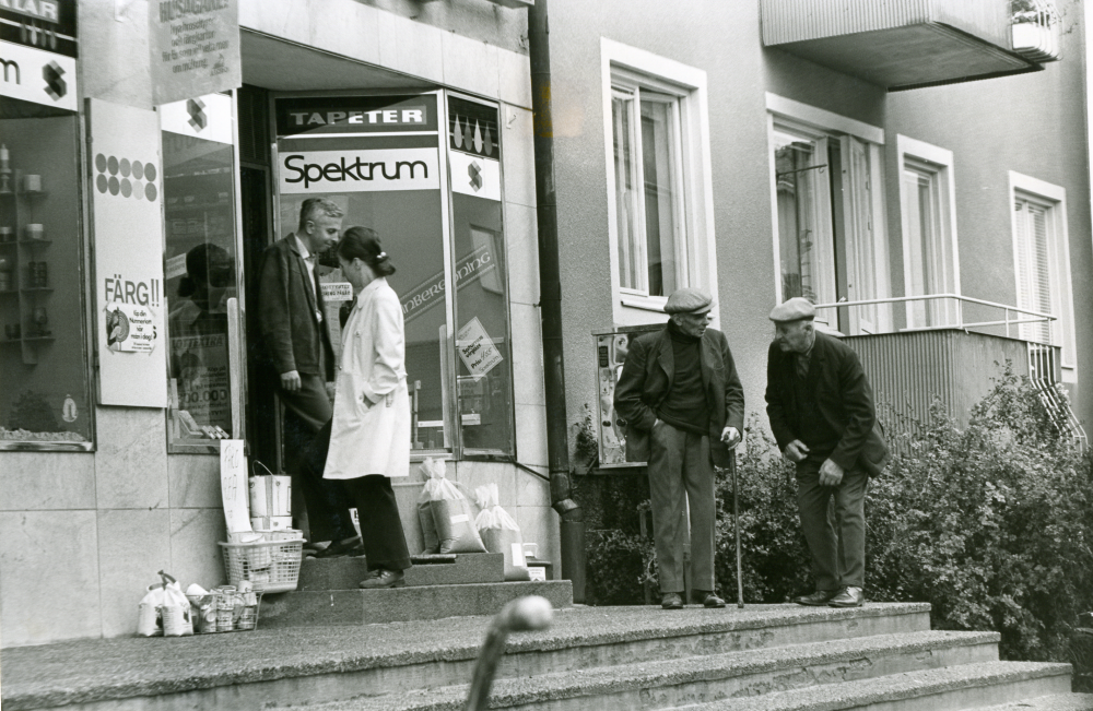 Kunder utanför Hans Uhrenius färgaffär på Centralvägen. 

•Fotografiet ingår i bildserien ”Vardagsliv i Vallentuna kommun” av Rachael Gough-Azmier & Gunilla Blomé, Haga Studios HB.