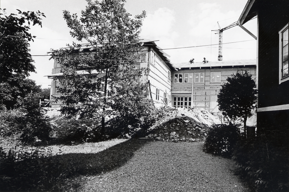 Det nya församlingshemmet Mathiasgården byggs mellan Klockargården och prästgårdsarrenatorns bostad. Utsikt över bygget från väster.  Huset har fått tak.  T h skymtar gaveln på arrendatorsbostaden