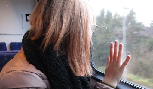 En kvinna sitter och tittar ut genom ett tågfönster. Hon har sin hand på fönsterrutan.