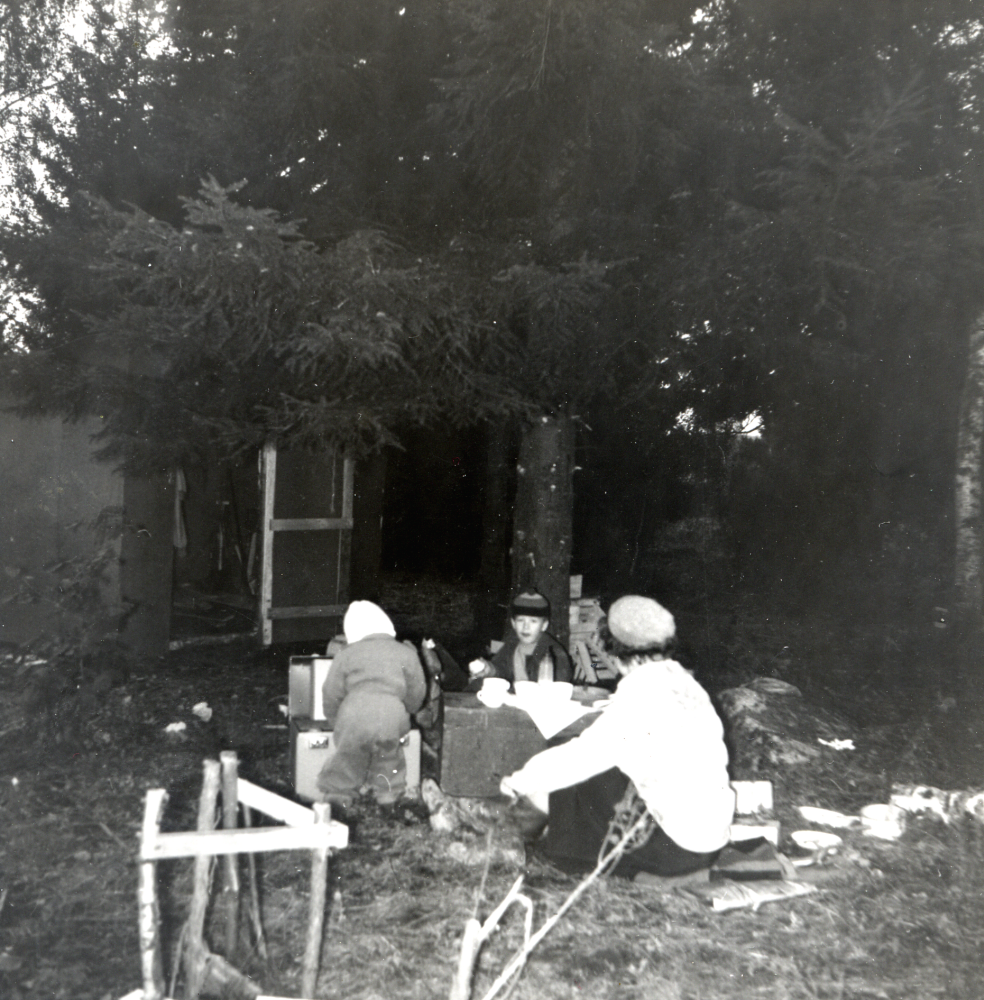 Norrängsvägen 5, familjen Ulla och Bengt Gustafson med barnen Lena, Sten och Tove, bygger nytt hus.  "Nybyggarna", äter sen middag hösten 1957.  På kortet står skrivet "Sen middag under granen.  Tove vid "färdkamraten", Sten och Ulla.  Boden skymtar"