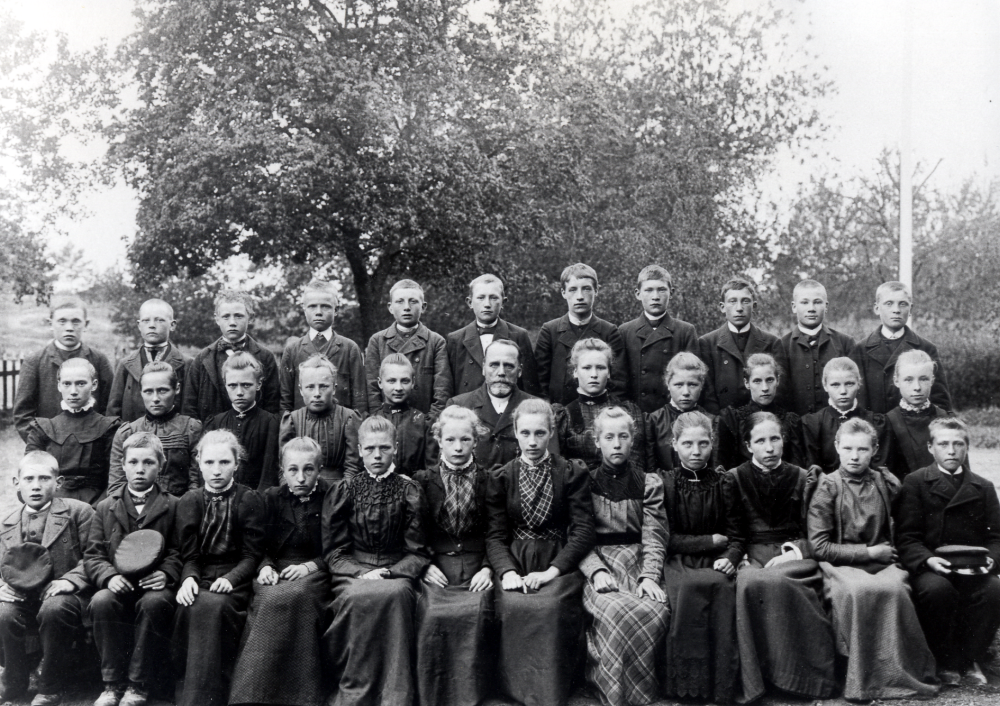 Kyrkoherde Karl Hedén med sina konfirmander.  Ett av barnen är syskonen Söderberg i Klockarborg.  De nio syskonen konfirmerades 1890 till 1908