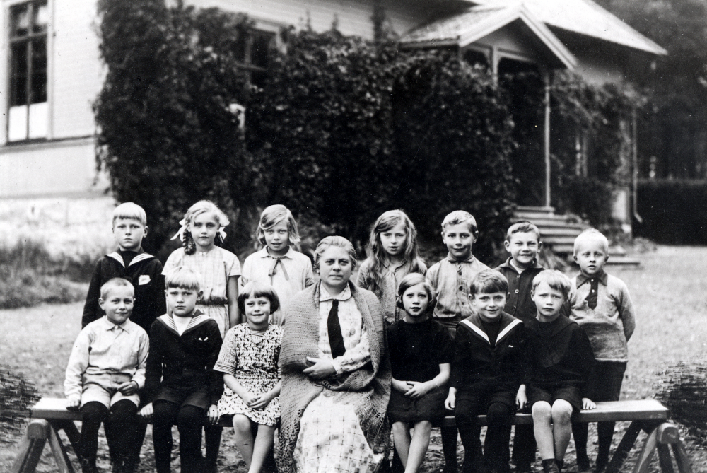 Lärarinnan Lisa Barthelsson tillsammans med barnen utanför Sunnanå småskola i Frösunda. I övre raden klass 2 fr v Martin Pettersson, Karin Sjöberg, Kerstin Helgöstam, Elly Strengbom, Karl-Erik Lundkvist, Nils Bohman? och Sigurd Eriksson. Nedre raden fr v klass 1 (utom Alva Franzén), Bengt Larsson, Harry Öhrlund, Rut Hollander, Alva Franzén, Stig Strengbom och Alf Franzén