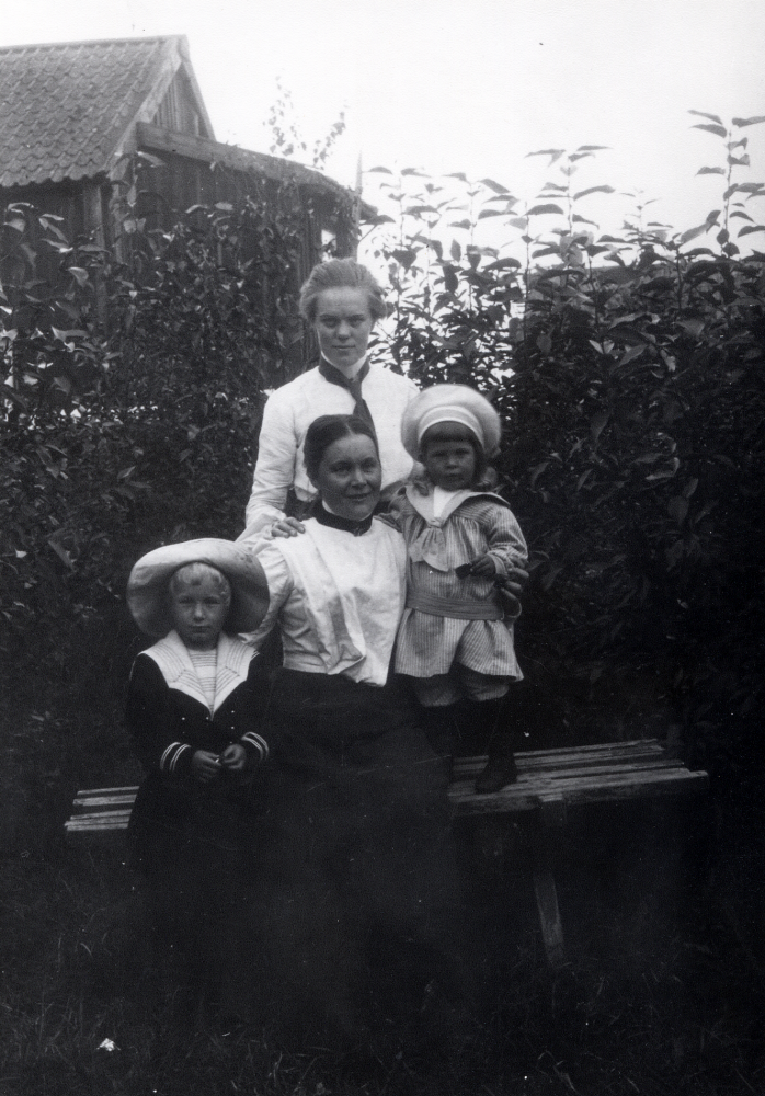 Maria Almén,Toftesta gård, med barnen Erik och Lennart , stående på bänken, samt Elin Nylund stående bakom Maria.  Elin var Marias kusin.  Byggnaden i bakgrunden är riven