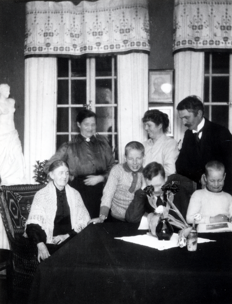 Familjen C M Carlsson från Solsta i Ormsta på Karlbergsvägen 41, 3 trappor i Stockholm. Fr v sitter Hans Uhrenius' farmor Anna Lovisa Johannesdotter Carlsson, 1847-1926, Hans' mor Hilda Maria Carlsson, född Westman, 5 maj 1881-21 april 1969, Max Lennart Carlsson, 29 april 1911-26 juli 1983, fastern Marie-Louise Schram, född Carlsson, 19 april 1876-14 oktober 1960. Fadern Carl Mattias Carlsson, 15 maj 1881-22 februari 1941, Hans Carolus Carlsson, 5 maj 1907-12 februari 1967 och Bo Fredrik Carlsson, 8 februari 1914-. Sönerna Hans, Lennart och Bo antog släktnamnet Uhrenius. Pojkarna var söner till C M Carlsson och hans hustru Hilda.