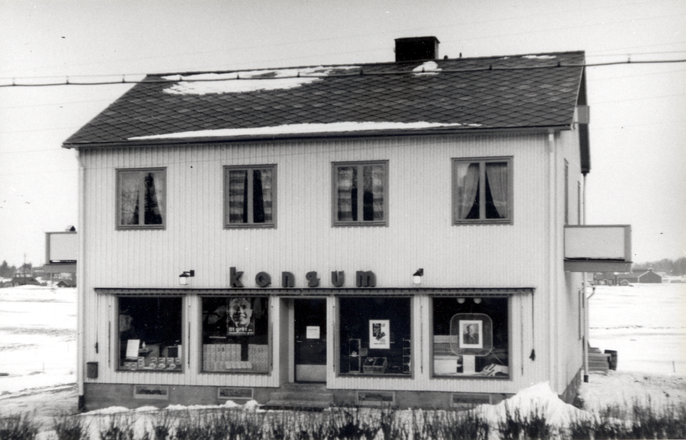 Konsums nya butik i Vallentuna. Huset byggdes 1939 och ingick i Konsumentföreningen Väsby med omnejd u p a som butik nr 6. Vallentunas första Konsumbutik öppnade 1933 och låg mitt emot den nya lokalen. Dessförinnan körde en varubuss en gång i veckan till kunder i Vallentuna. Rickard Andersson startade kooperationen tillsammans med 56 andra blivande medlemmar i Vallentuna. I bakgrunden t h om huset syns Åby tegelbruk. 1965 använder Konsumhuset som tillfällig skollokal. Se Konsum i norrort 1907-1997, s 29-30