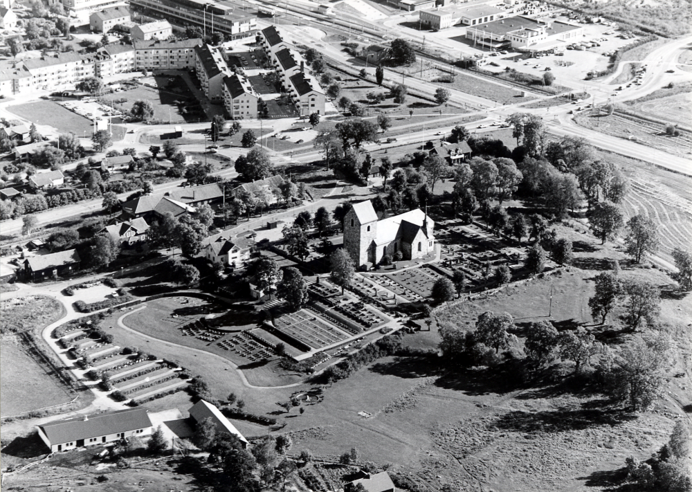 Flygfoto över Vallentuna kyrka och Vallentuna centrala delar.  I förgrundens syns taket på Sjövillan, i bildens mitt bostadshusen längs Centralvägen med Tuna torg och Tunahuset bakom det.  T h syns korsningen Roslagsbanan och Angarnsvägen, samt korsningen Väsbyvägen och Stockholmsvägen och industriområdet öster om järnvägen