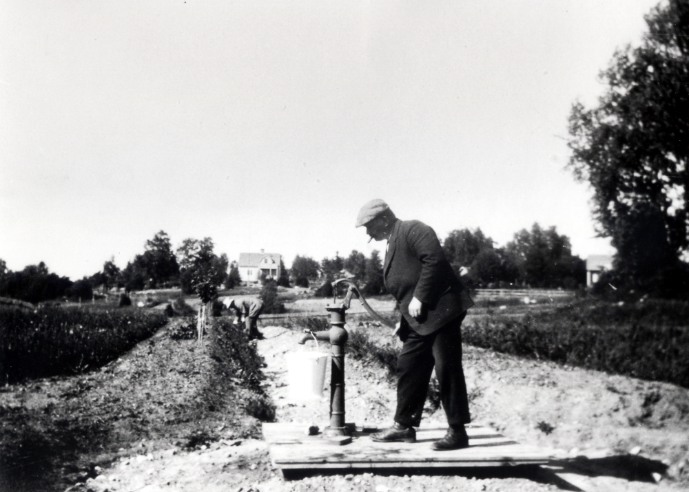 Claës Erik Schram köpte 1921 tomtmark öster om Ormsta gård för att bygga ett sommarställe.  Det fick namnet Schramsta.  Sommaren 1923 är huset färdigbyggt.  Samtidigt anlade Claës Erik Schram en trädgård med solur, blommor och fruktträd.  Här står ägaren och pumpar vatten i den nyanlagda trädgården.  I bakgrundens syns Solsta, bostad för svågern C M Carlsson och hans familj och t v Sigridslund, bostad för C J Pettersson "Brännar-Pelle" och hans familj