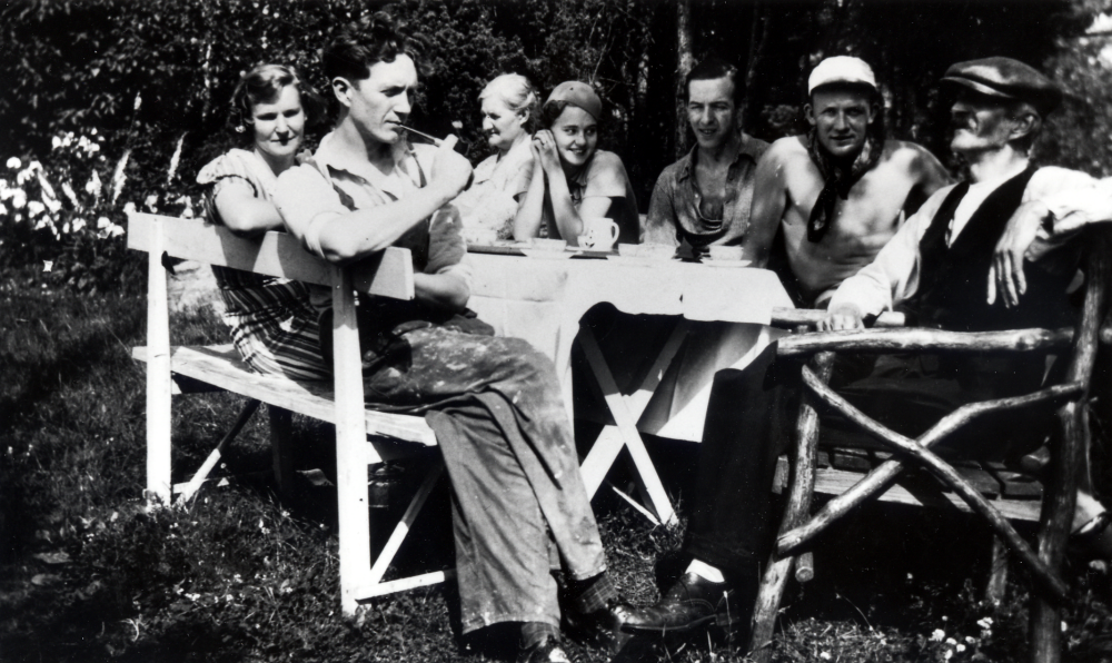 Kaffepaus på Solsta i Ormsta.  Runt kaffebordet sitter Märta och Hans Uhrenius på bänken, paret flyttade till sitt nybyggda hus på Solstas tomtmark hösten 1938.  På andra sidan bordet sitter fr v  Hilda Carlsson, Hans mamma, förmodligen en fästmö till Tore Glassel, Lennart Uhrenius, Tore Glassel och Hans pappa, konstnären Carl Mattias Carlsson.  Hildas och C M: s tre pojkar Hans, Bo och Lennart tog namnet Uhrenius (efter Uhre som tidigare fanns i släkten)