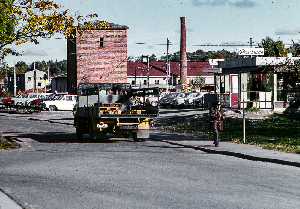 Banvägen med Pressbyrån till höger. Den höga röda tegelbyggnaden hörde till järnvägen, möjligen var den kvar från tiden då man behövde vatten till ångloken. Den långa byggnaden med ljus fasad är Vallentuna tegelbruk. 
Bildserie: Vallentuna på 1960-talet.