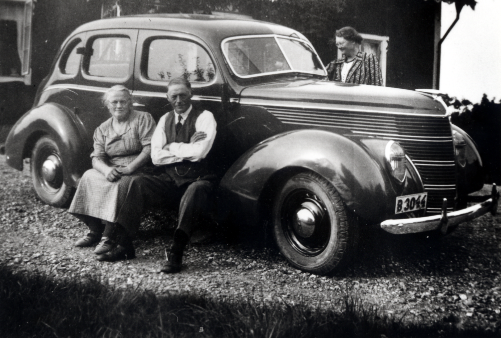 Carl J Lillje med hustrun Linnea sitter på fotsteget på första bilen, en Ford från 1936, utanför Sunnarby  gård i Kårsta.  Damen på bilens högra sida är Anna-Lisa Nilssons mamma från Stockholm