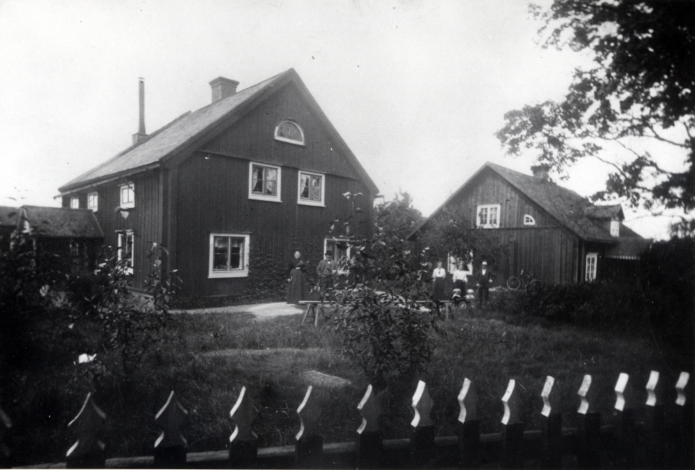 Mellangården och Södergården t h i Toftesta, Össeby-Garn. Framför husen står fr v Karolina Pettersson (Lennart Alméns mormor), Gustaf Almén, okänd, okänd, okänd. Erik Almén och Lennart Almén är de små barnen i skrindan