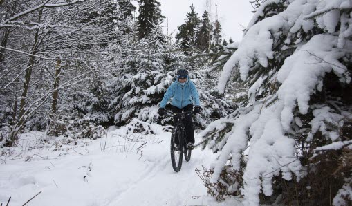 Cyklist som cyklar i skogen. På marken och träden är det snö. 