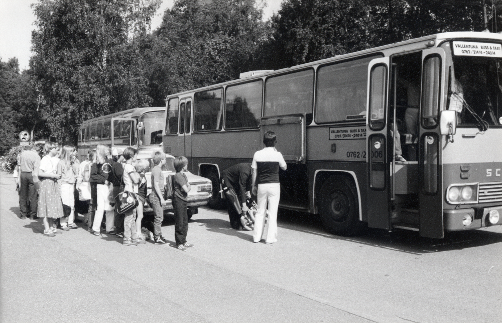 Klasserna 4 ka-4 kc i Karlbergsskolan är på väg till Vira bruk och Vaxholms fästning på skolresa.  Busschauffören fäller ihop Anders Blombergs rullstol, läraren Kenneth Palmqvist står vid bussen.  Främst i ledet som väntar på att få kliva ombord på bussen står fr h Fredrik Sandberg och Klas Hansén