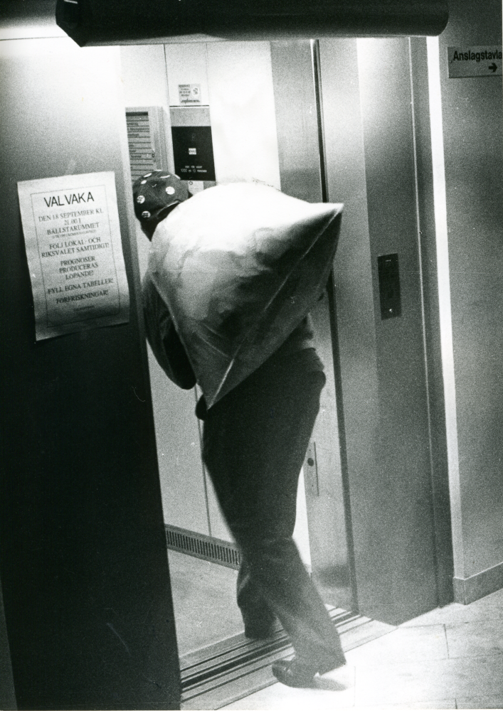 Val 1988. En säck med valsedlar bärs in i hissen i kommunalhuset. På väggen sitter ett anslag om  "Valvaka i Bällstarummet kl 21".