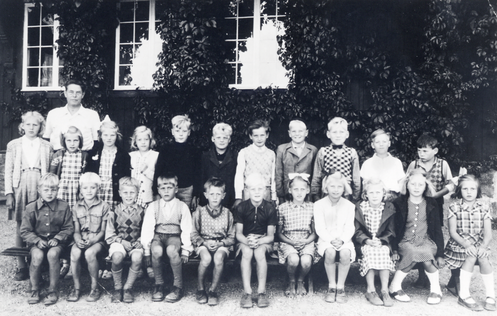 Läraren Josef Andersson tillsammans med skolbarnen utanför Hjälmsta skola Röda skolan. Övre raden fr v Ulla Leverin, Mona Bergström, Siv Österberg, Birgitta Bengtsson, Bengt Nyberg, Olof Lindblom, Lage Jansson, Tommy Karlsson, Gunvor Nilsson och Leif Hallén. Sittande fr v Bertil Wahlgren, Björn Rundquist, Kjell Pettersson, Björn Gustafsson, Ralf Sundqvist, Rune Lundquist, Gunborg Jansson, Ingegerd Tillborg, Ulla Brolin, Harriet Raab och Ing-Britt Karlsson