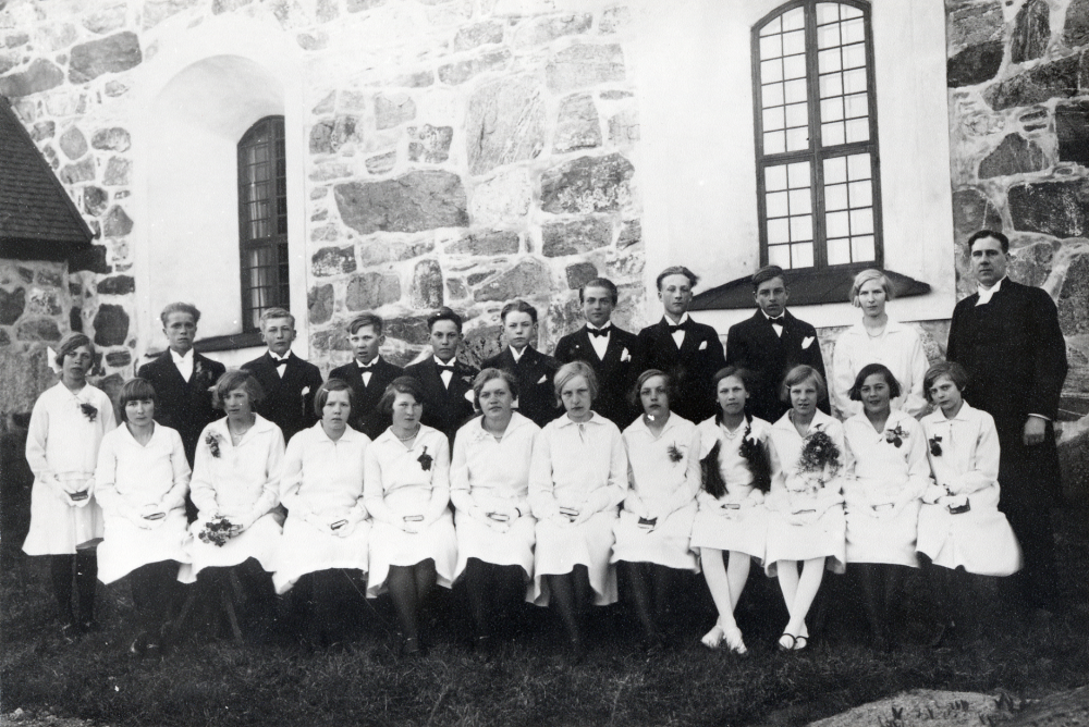 Konfirmation i Kårsta kyrka.  Kyrkoherde Paul Sjöberg tillsammans med konfirmanderna vid kyrkan.  Övre raden fr v Lennart Ström, Sven Ländin, Ivar Söderström, Stig Söderström, Sixten Lundin, Gunnar Nyberg, okänd, Ernst Söderberg och Anna-Lisa Wallén.  Nedersta raden fr v Greta Jansson, Vivi ?, Svea Jansson, ? Söderblom, Signe Karlsson, Elsa Karlsson, Vera Lind,  Elsa Karlsson, Gunborg Jansson, ?Forsman, Alfhild Eriksson, Anna-Britta Sandgren