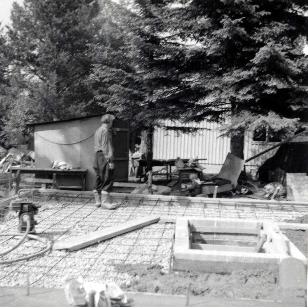 Norrängsvägen 5 - bottenplattan gjuts.  I grunden står      .  T v "vår lilla bod under granen".  I villan i bakgrunden, Norrängsvägen 7, bor familjen Pernbom