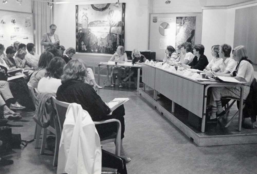 Valdebatt 1985. Sju partiers kvinnliga representanter möts för att diskutera politik, främst familjepolitik, inför valet. I panelen fr v Carin Adlercreutz ordförande, Ingrid Ullman sekreterare, Lena Gunnerblad skp, Lena Lundgren vpk, Sylvia Pettersson s, Elisabeth Odell kds, Margareta Lundberg mp, Marianne Holmbom c och Margareta Gustavsson m. Stående man är Tore Hjerpe. Debatten ägde rum i Vallentunasalen.