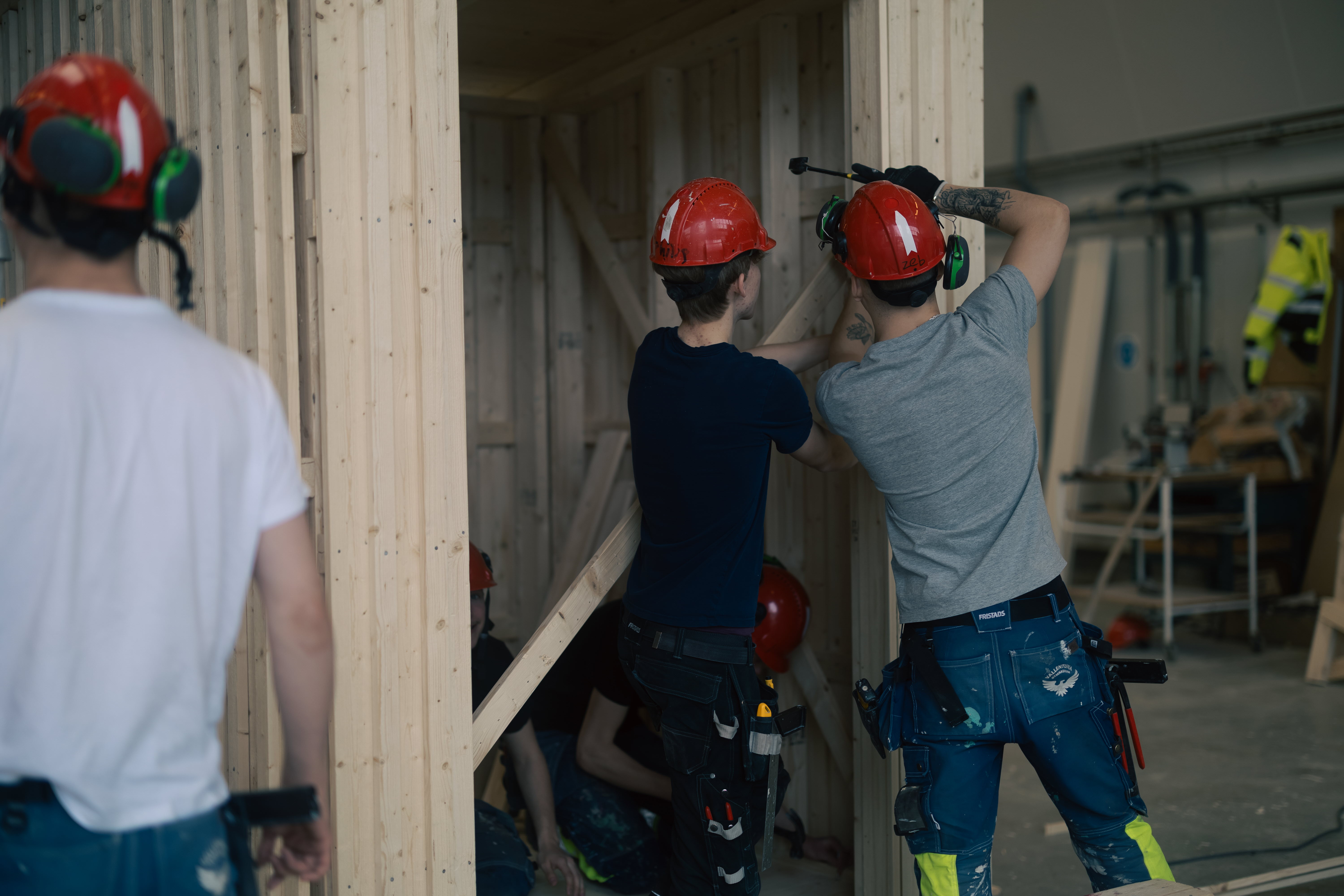 Två elever hjälps åt med att hamra fast en bräda till ett pågående bygge i form av ett modulhus. En tredje elever står i bakgrunden och betraktar bygget.